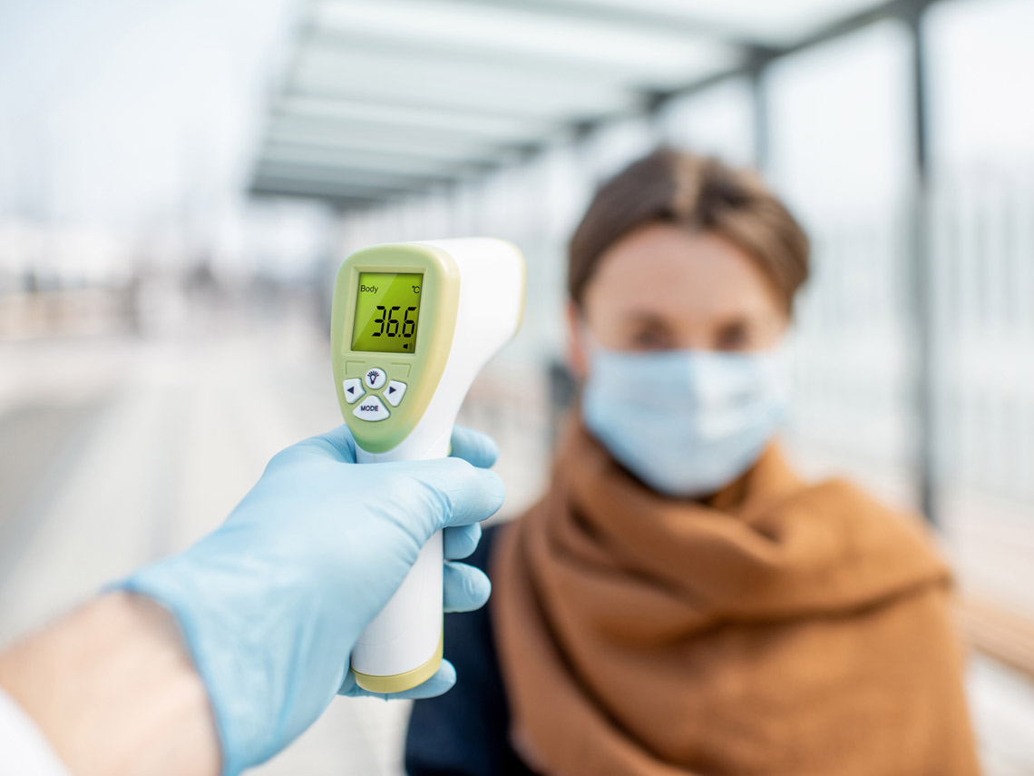 Hombre tomándole la temperatura a una mujer con mascarilla