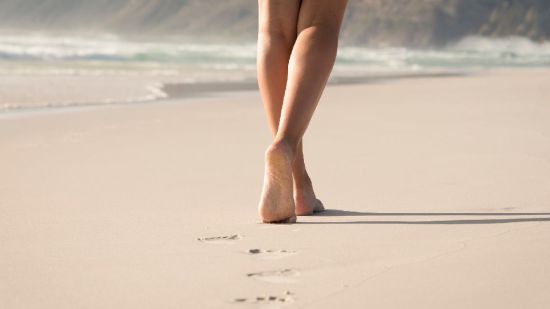 Mujer descalza andando por una playa