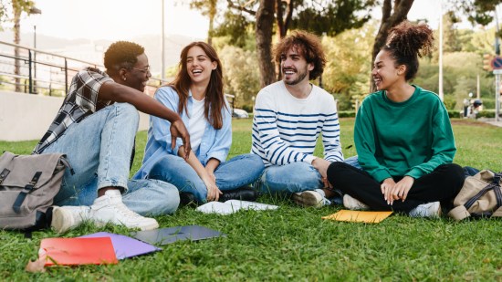 Amigos estudiantes universitarios sentados en el césped, hablando en el campus universitario