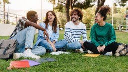 Amigos estudiantes universitarios sentados en el césped, hablando en el campus universitario
