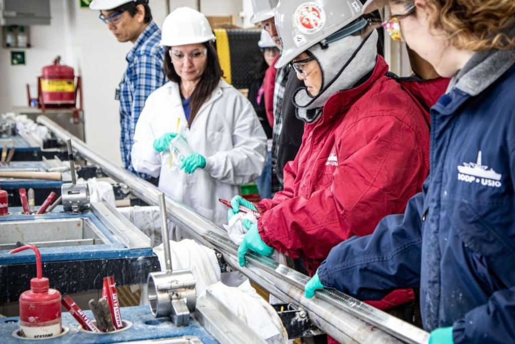 Chieh Peng, oficial de laboratorio del IODP JRSO, vestido con una chaqueta roja, trabaja junto a Kara Vadman, especialista en laboratorio marino, para determinar los puntos de corte en las secciones del núcleo