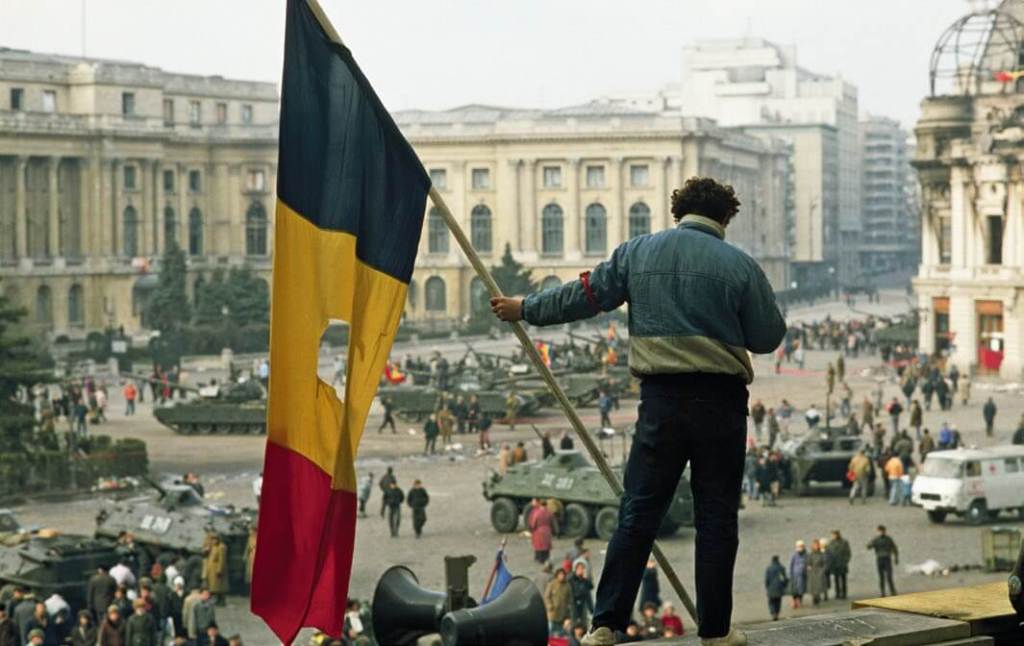 Un hombre con una bandera rumana con el emblema comunista arrancado