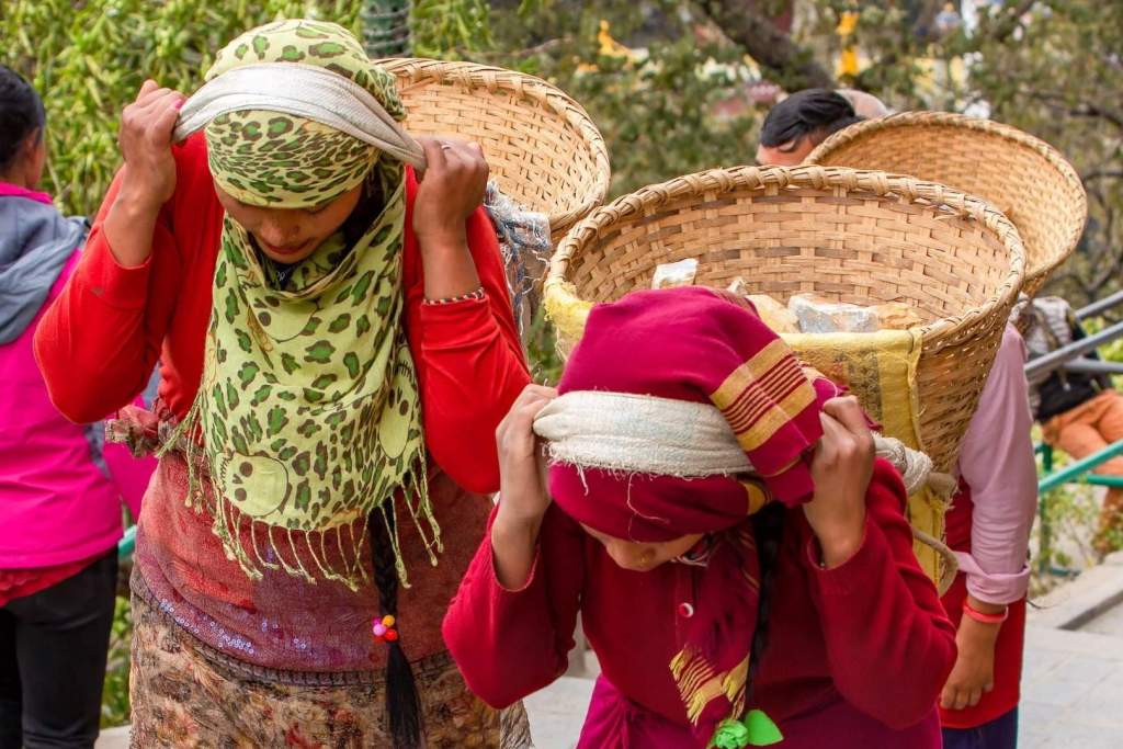 Mujeres nepalesas actuales transportan cestas pesadas utilizando correas que se ajustan a la frente, una técnica ancestral aún en uso en regiones rurales