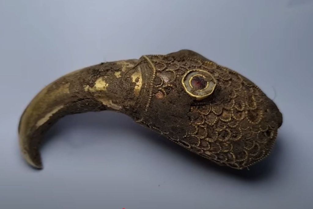 La pieza tras su limpieza inicial: se observa con mayor claridad la intrincada decoración de escamas y el ojo engastado en granate, lo que confirma su manufactura exquisita y simbolismo ritual