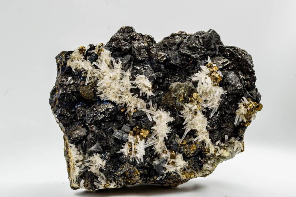 Esfalerita (gris oscuro) con pirita (cristales estriados dorados), calcopirita (dorado verdoso) y cuarzo (cristales blancos). Colección de Mineralogía de la Facultad de Geológicas (UCM). Foto: G. Pinto.