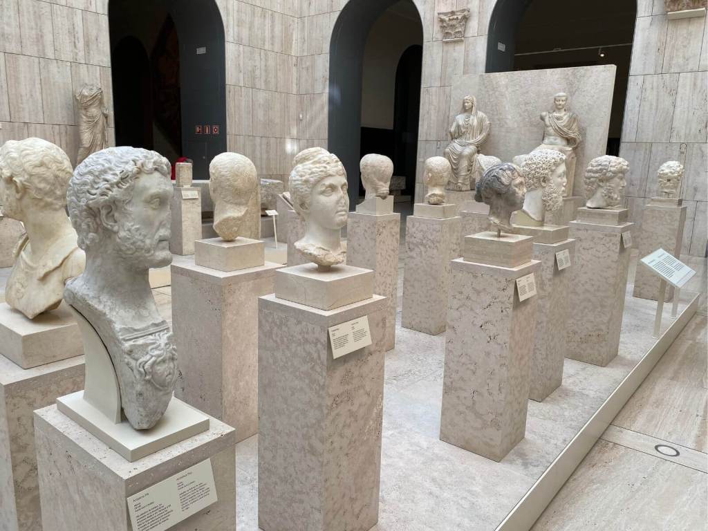 5.	Retratos romanos en el Museo Arqueológico Nacional, Madrid. Foto propia. Mientras paseamos por la Plaza de Colón o por la calle Serrano, podemos entrar unos instantes al MAN en Madrid y toparnos con rostros de notables, aristócratas y emperadores romanos que quedaron inmortalizados en piedra en Hispania. Son el eco en piedra de un mundo que se fue, pero que aún flota en nuestra atmósfera.