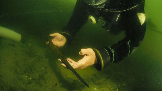 Un arqueólogo subacuático recupera una punta de lanza medieval del fondo del lago Lednica, en Polonia